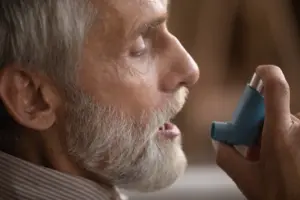 Older man using inhaler for asthma-related nasal congestion and shortness of breath