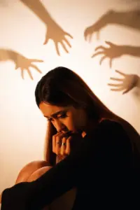 A distressed woman sitting alone with shadowy hands reaching toward her, symbolizing emotional trauma, anxiety, and psychological distress. -Symptoms of PTSD