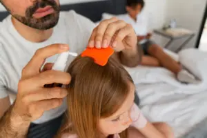 A parent using a fine-tooth comb and topical solution on a child’s scalp to remove head lice. This image supports content about ivermectin for skin, showing its use as a treatment option for parasitic infestations like head lice.