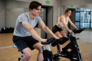 This image shows indoor cycling, a cardio workout that helps burn calories, improve metabolism, and support fat loss in the FUPA (Fat Upper Pubic Area) over time.